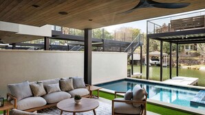 A modern outdoor living area with a pool, a sofa set, and a dining table. - Luxury 3-Story Lakehouse |Pool + Hot Tub + Sundeck (Horseshoe Bay)