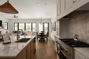 Een moderne keuken met een groot eiland, een eethoek met tafel en stoelen, en een woonkamer met een bank en grote ramen.