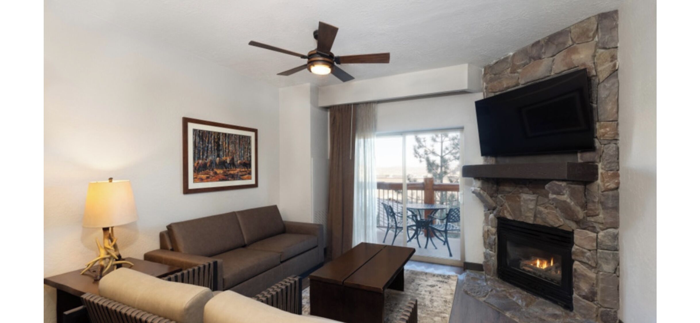 A living room with a stone fireplace, a ceiling fan, a sofa, a coffee table, and a TV mounted on the wall.