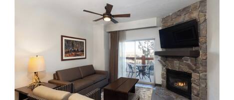 A living room with a stone fireplace, a ceiling fan, a sofa, a coffee table, and a TV mounted on the wall.