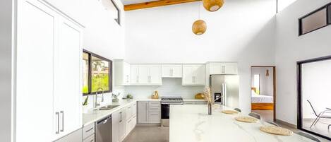 Une cuisine moderne avec des meubles blancs, un îlot en marbre et des poutres en bois au plafond.