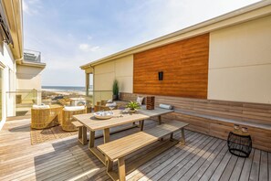 A wooden deck with a table and benches, a potted plant, and a view of the ocean. - Oceanfront 3BR Condo, Huge Private Deck, Pool, Hot Tub, Elevator, Steps to Beach (Carolina Beach)