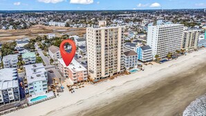 Ein Küstenhotelbereich mit mehreren Gebäuden, einem Strand und einem roten Standortmarker.