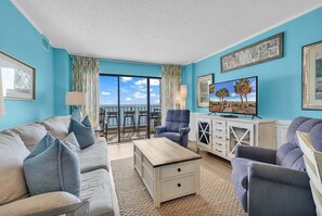 A living room with a sofa, armchairs, a coffee table, and a TV. There is a balcony with a view of the ocean. - Atalaya Towers 1004 - Oceanfront in Garden City Beach (Garden City Beach)