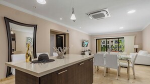 Una cocina moderna con una isla central, comedor con mobiliario blanco y un ventanal con vistas a zonas verdes.