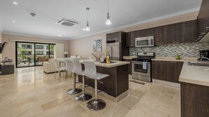 Una cocina moderna con una isla central, electrodomésticos de acero inoxidable y un comedor con taburetes de bar.