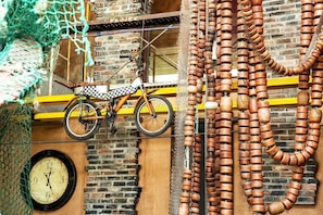 Una bicicleta apoyada en un muro de ladrillo, un reloj y varios objetos de madera colgados en la pared.