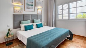 Ein Schlafzimmer mit einem Bett, einem Nachttisch, einem Fenster mit Jalousien und Wandbildern.