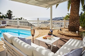 A poolside area with a white outdoor seating area, a table with food and drinks, and a view of the sea. - Stunning Villa with Breathtaking Ocean View (Mogán)