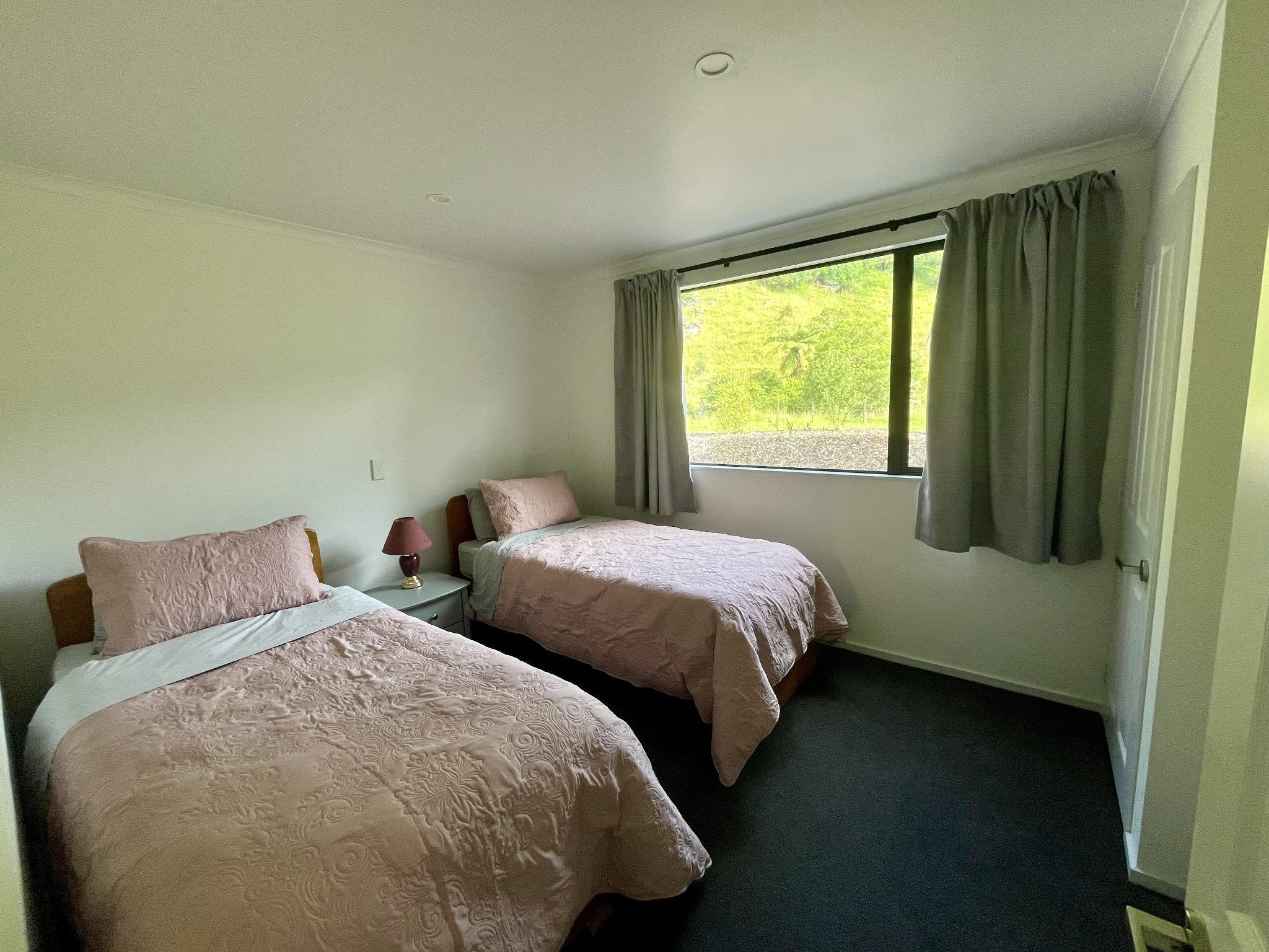 A room with two beds, a nightstand, a lamp, and a window with curtains.