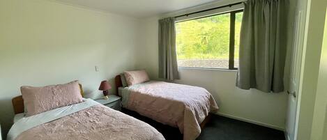 A room with two beds, a nightstand, a lamp, and a window with curtains.