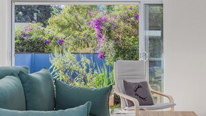 A room with a sofa, a chair, a small table, and a view of a garden through a glass door. - Macadamia Ocean Escape (Pottsville)