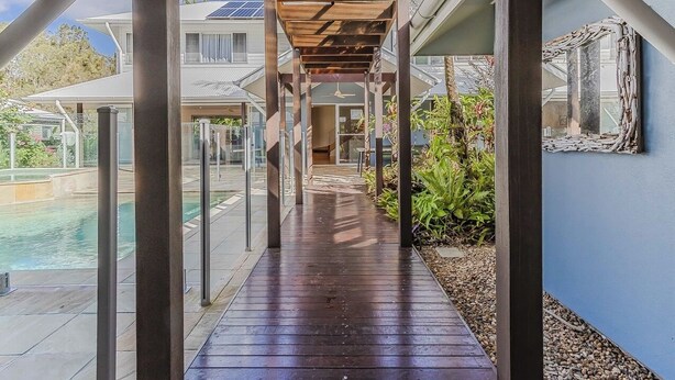 A covered outdoor walkway leading to a pool, with a view of a house and greenery. - Macadamia Ocean Escape (Pottsville)