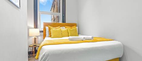 Habitación de hotel con cama, ventana, lámpara y un cuadro en la pared.