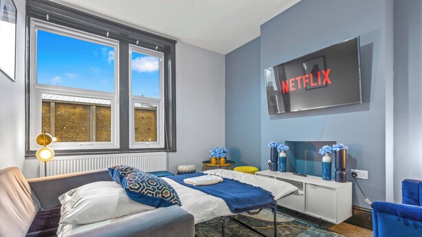 A modern bedroom with a bed, bedside tables, a TV, and a window with a view. - Gorgeous 2BR flat in Fulham & Chelsea (London)