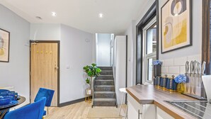 A modern kitchen with a wooden countertop, a dining area with blue chairs, and a staircase leading to another level. - Gorgeous 2BR flat in Fulham & Chelsea (London)
