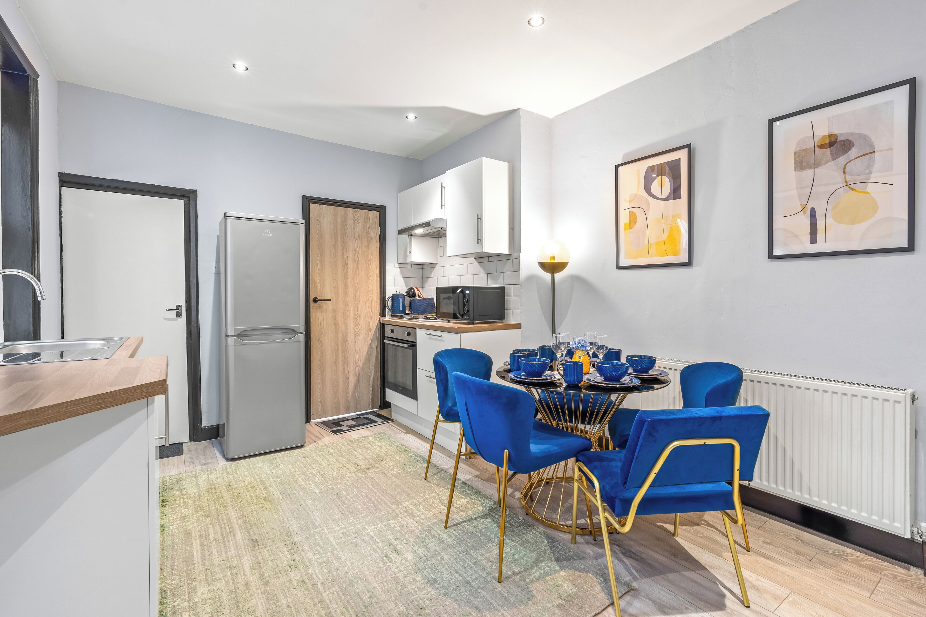 Une cuisine moderne avec un coin repas, des meubles blancs, un réfrigérateur et une table avec des chaises bleues.