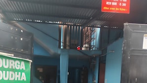 A room with a blue wall, a table with a chair, a red sign, and a large black container. - Anand Home Stay (Kathmandu)