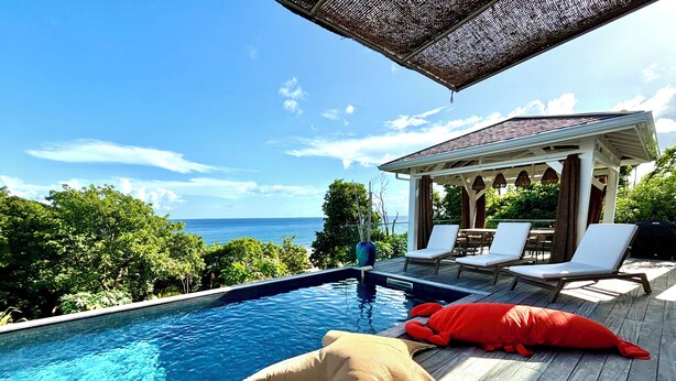 Eine Holzterrasse mit Pool, Liegestühlen und Meerblick.