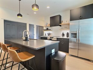 Une cuisine moderne dotée d’un îlot central, de tabourets de bar, d’un réfrigérateur en acier inoxydable et de luminaires suspendus.