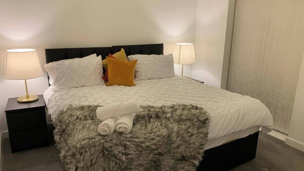 Ein ordentlich bezogenes Bett mit einer flauschigen Decke, zwei Nachttischlampen und einem Kopfteil.