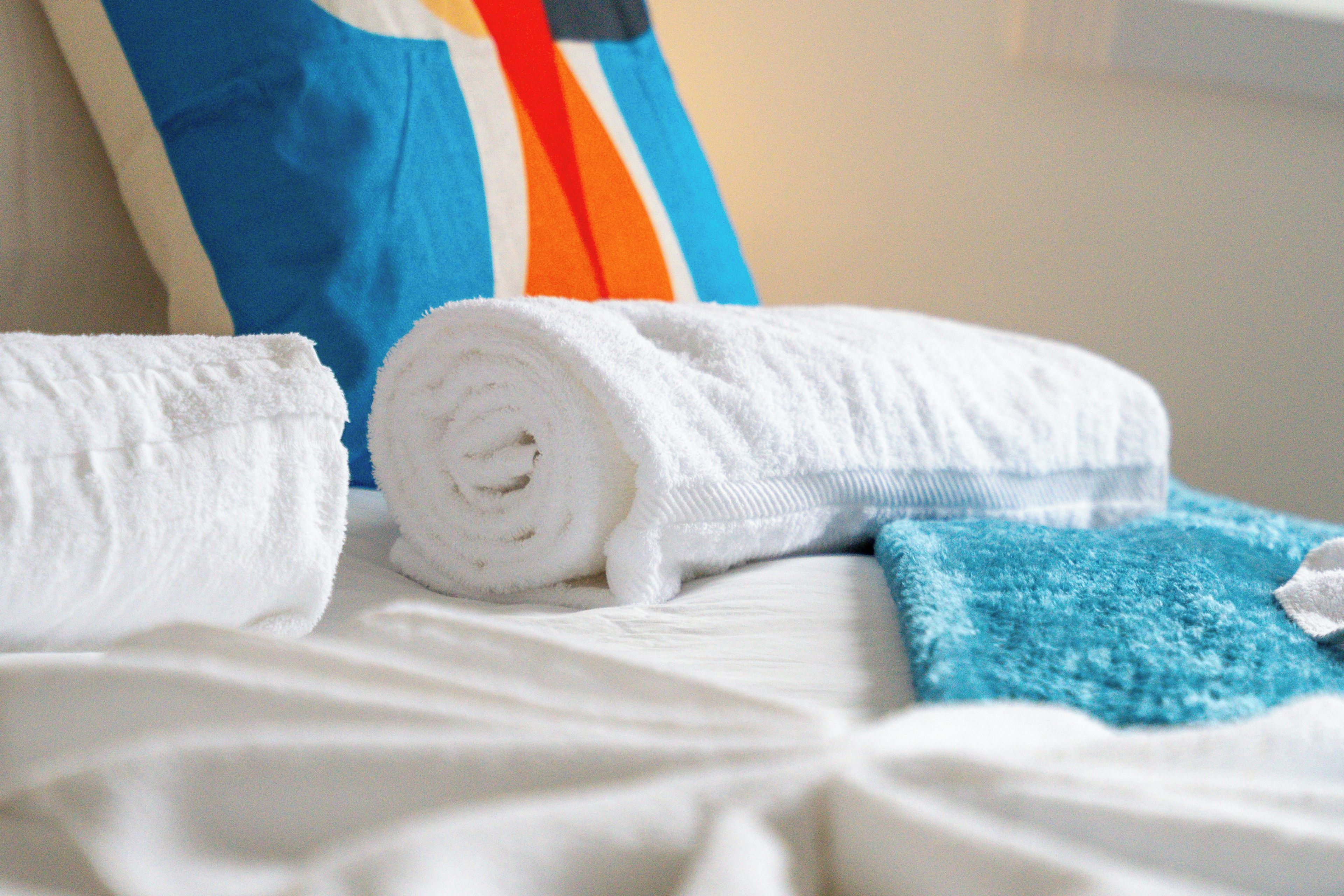 Una cama con sábanas blancas y toallas enrolladas.