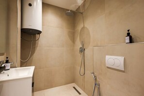 Une salle de bain avec un lavabo blanc, un distributeur de savon manuel, une pomme de douche à main et un radiateur fixé au mur.
