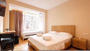 Habitación de hotel con cama, escritorio, silla, mesita de noche y ventana con cortinas.