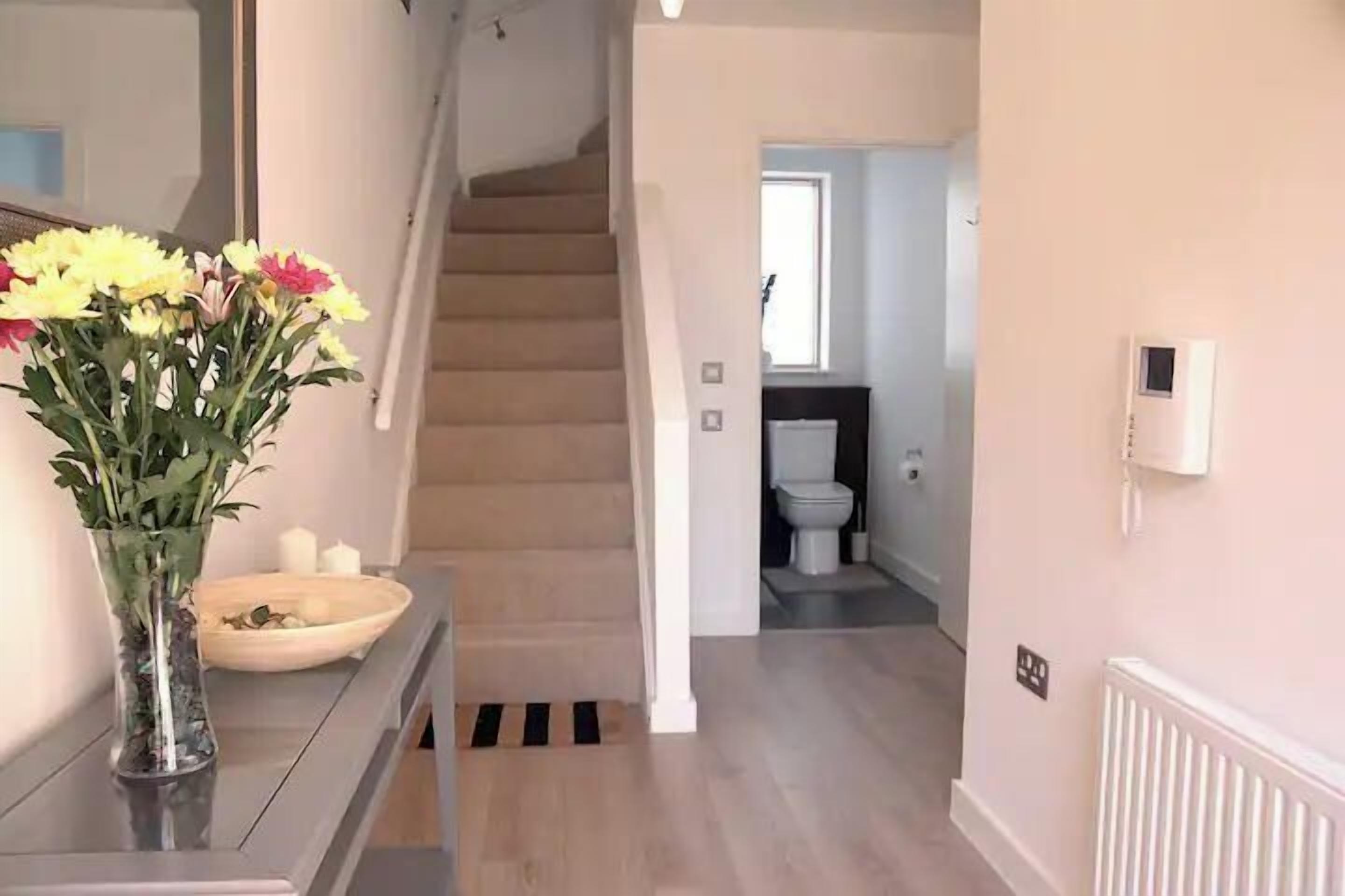 A modern interior with a staircase, a bathroom, and a vase with flowers on a counter.