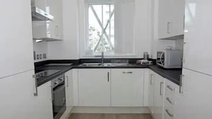 Una cocina moderna con armarios blancos, encimera negra, ventana con refuerzos cruzados y un microondas.