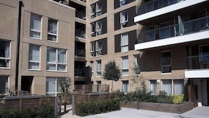 Un edificio residencial de varios pisos con balcones, un pequeño jardín y un camino pavimentado.