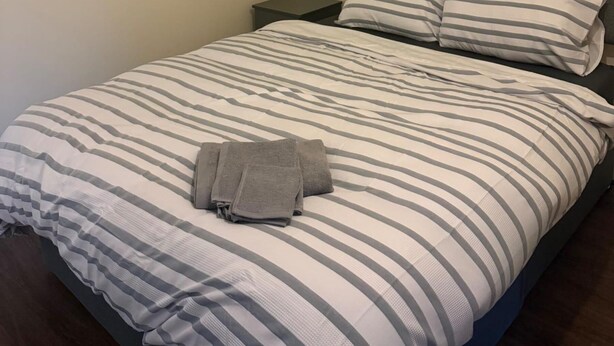 Een bed met gestreken beddengoed en een opgevouwen handdoek erop.