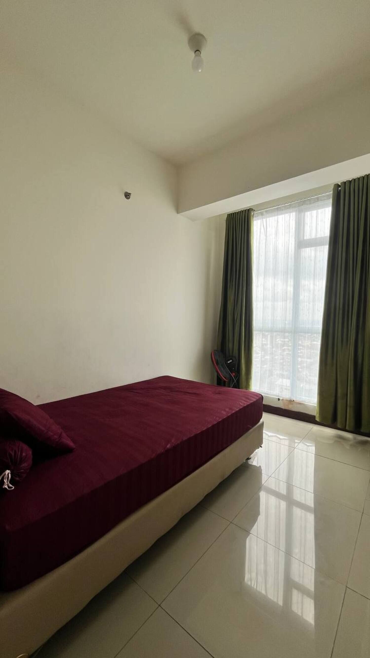 Una habitación con una cama, una ventana con cortinas, una lámpara en el techo y suelo de baldosas.