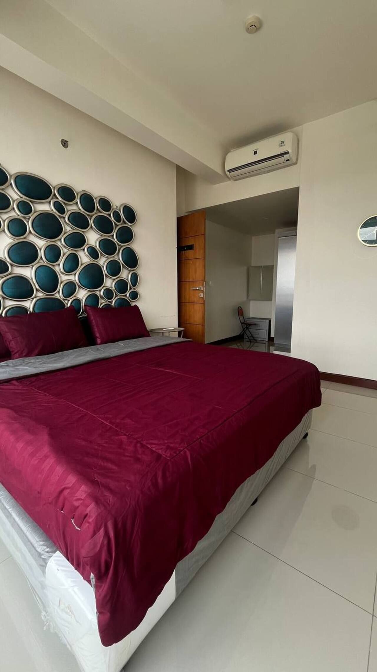 Een slaapkamer met een bed, een wandairconditioner, een houten kledingkast en een kleine tafel.