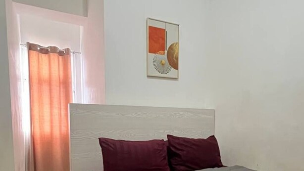 Ein Schlafzimmer mit Bett, Kopfteil, Wandbild und einem Vorhangfenster.