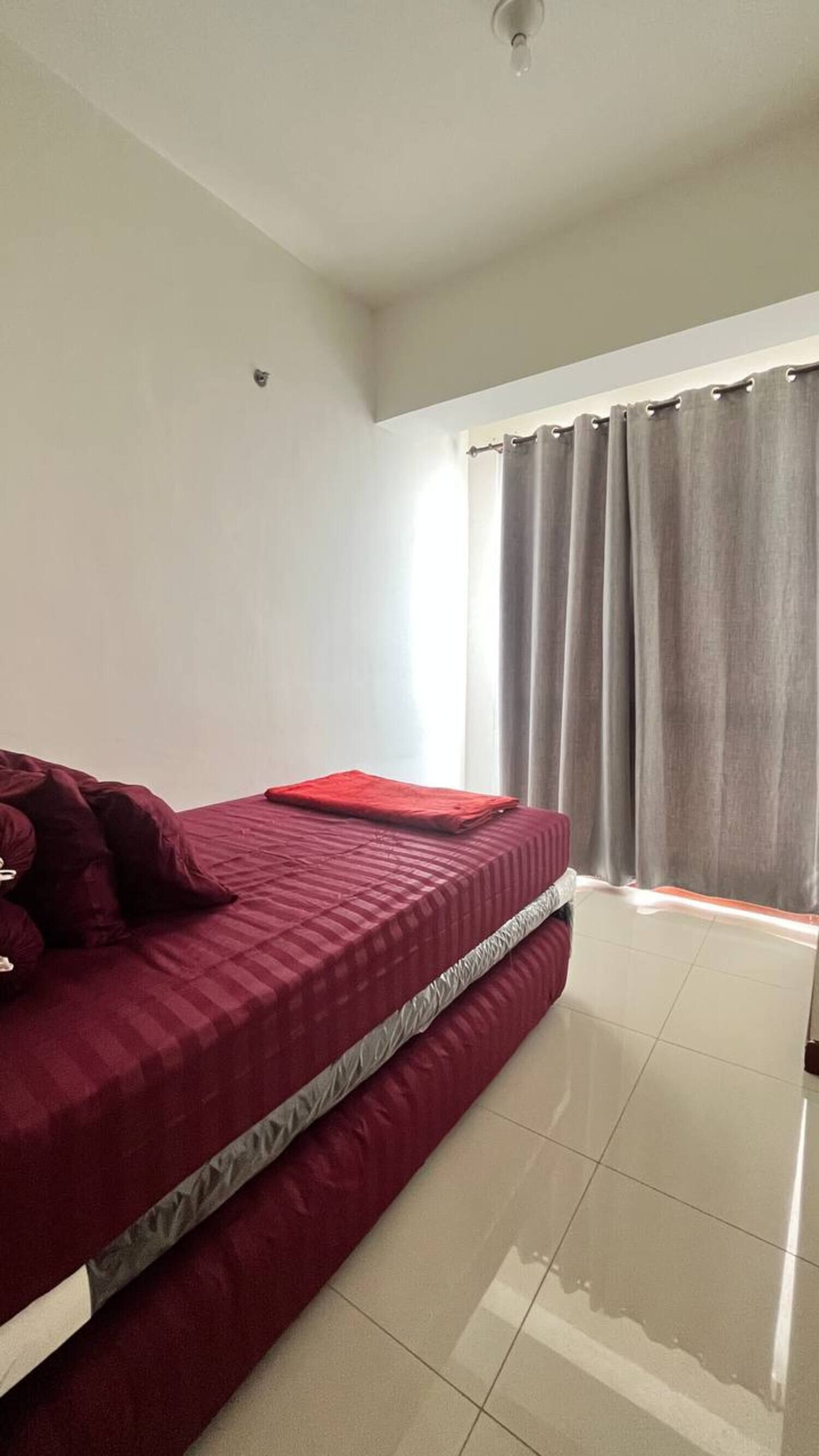A room with a bed, a window with curtains, and a ceiling light.