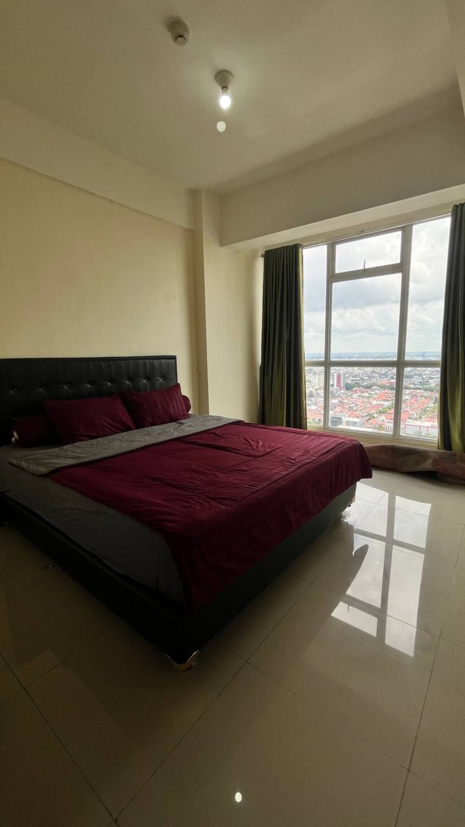 Quarto com uma cama grande, janela com cortinas e vista para a cidade.