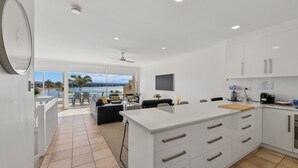 Una cocina moderna con armarios blancos, una isla grande y vistas a una piscina y palmeras.