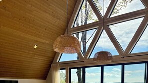 A modern kitchen with a large island, wooden ceiling, and large windows overlooking a lake. - Welcome to Torch Hill A-Frame, perched above iconic Torch Lake. (Alden)