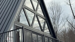A modern building with a triangular roof, large windows, and a wooden deck. - Welcome to Torch Hill A-Frame, perched above iconic Torch Lake. (Alden)