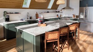 A modern kitchen with a large island, wooden ceiling, and pendant lighting. - Welcome to Torch Hill A-Frame, perched above iconic Torch Lake. (Alden)
