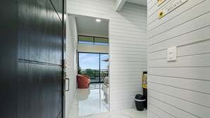 A modern interior with a dark wooden door, white walls, and a marble floor leading to a balcony with outdoor furniture. - The Honeybee House: Spacious 2BR Jungle Home (La Fortuna)
