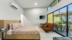 A modern bedroom with a bed, a sofa, a TV, and a balcony with outdoor furniture. - The Honeybee House: Spacious 2BR Jungle Home (La Fortuna)
