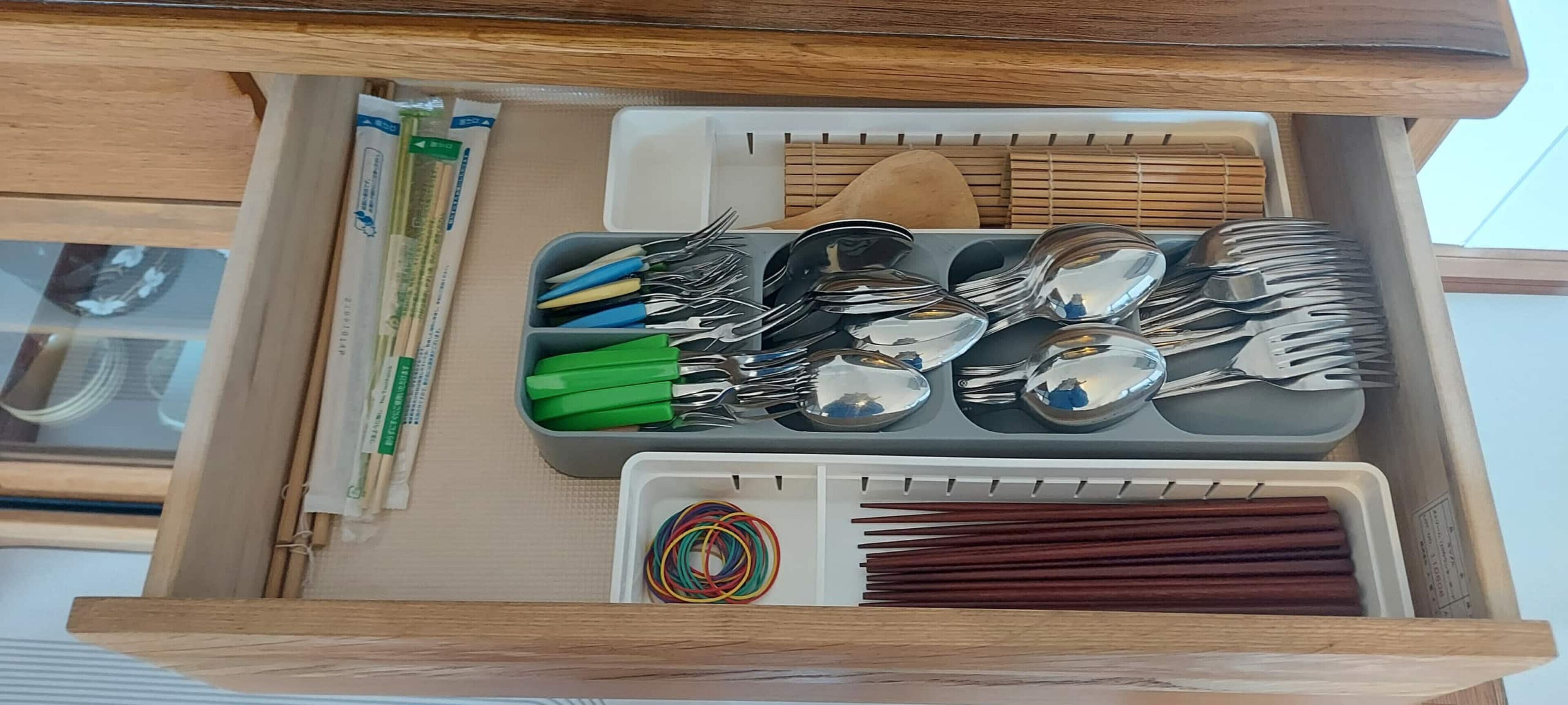 A drawer with utensils, chopsticks, and a plastic container.