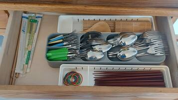 A drawer with utensils, chopsticks, and a plastic container.