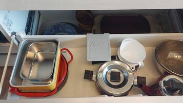 A kitchen drawer with various utensils and containers, including a metal strainer, a white bowl, and a red container.