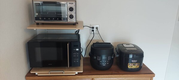 A kitchen counter with a microwave, toaster, coffee maker, and a rice cooker.