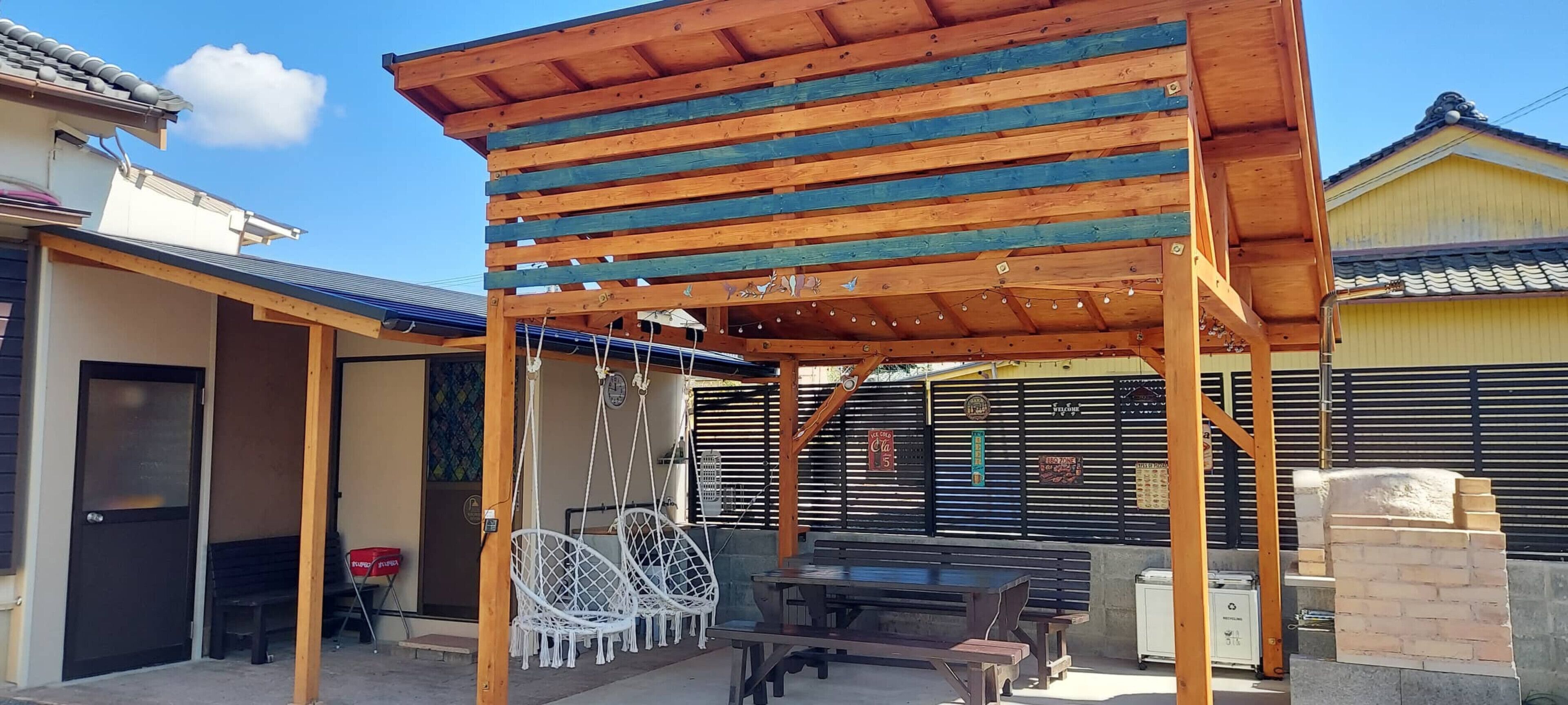 A covered outdoor seating area with a wooden pergola, a bench, and hanging chairs.