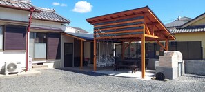 Zona relax esterna coperta con un pergolato in legno, un barbecue e una ventola.