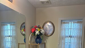 A bathroom with a white sink, a toilet, a mirror, and a vase with flowers. - Cozy 2-bedroom house in serene Stockbridge with AC (Stockbridge)